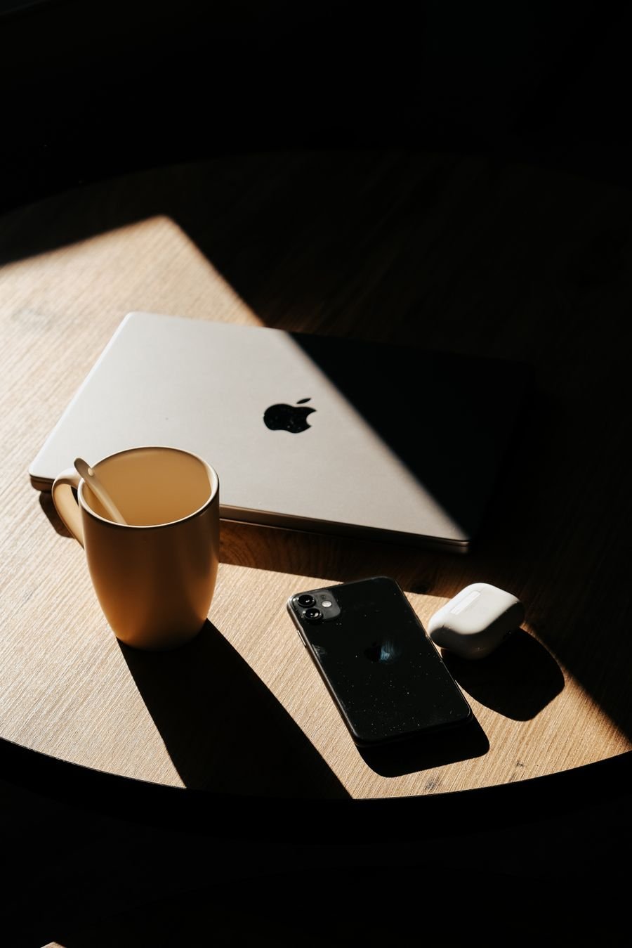 A closed laptop and phone on a sunlit wooden table, ready to upload a manuscript